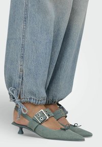 Světle modré denimové slingback boty s špičatou špičkou, nastavovacími přezkami a kitten podpatkem. V kombinaci s volnými světle modrými denimovými kalhotami.