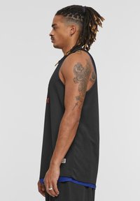 Svart basketballdrakt laget av pustende mesh-materiale, med blå kant nederst og et grafisk tatoveringdesign på armen.