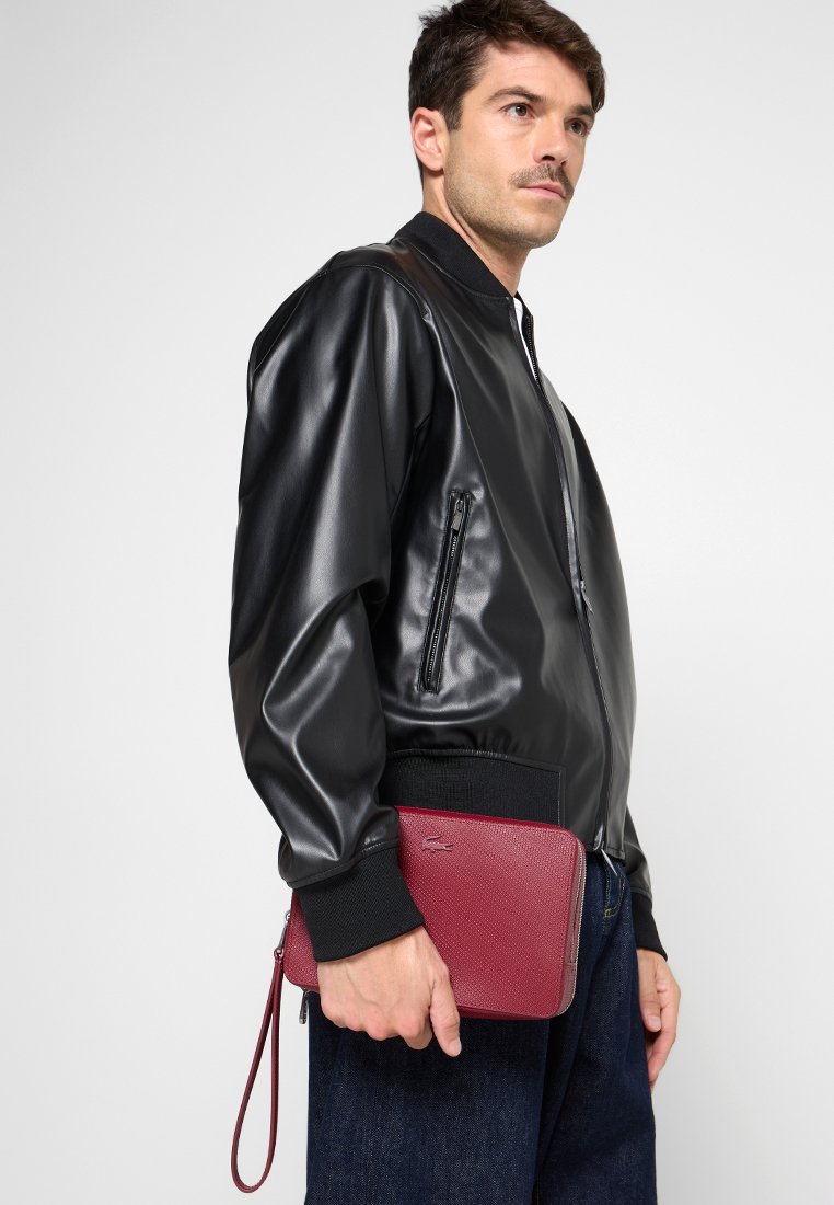 Veste bomber en simili cuir noir avec des poignets et un ourlet côtelés, associée à une pochette texturée bordeaux avec une sangle de poignet.