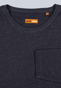 Dunkelblaues, strukturiertes T-Shirt mit Rundhalsausschnitt, ausgestattet mit einem orangefarbenen Etikett und einer Brusttasche. Der Stoff wirkt weich und leicht gemustert.