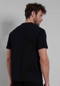 T-shirt nera in cotone con maniche corte, collo rotondo, texture liscia e un design semplice. La vista dal retro mostra una vestibilità classica e linee pulite.