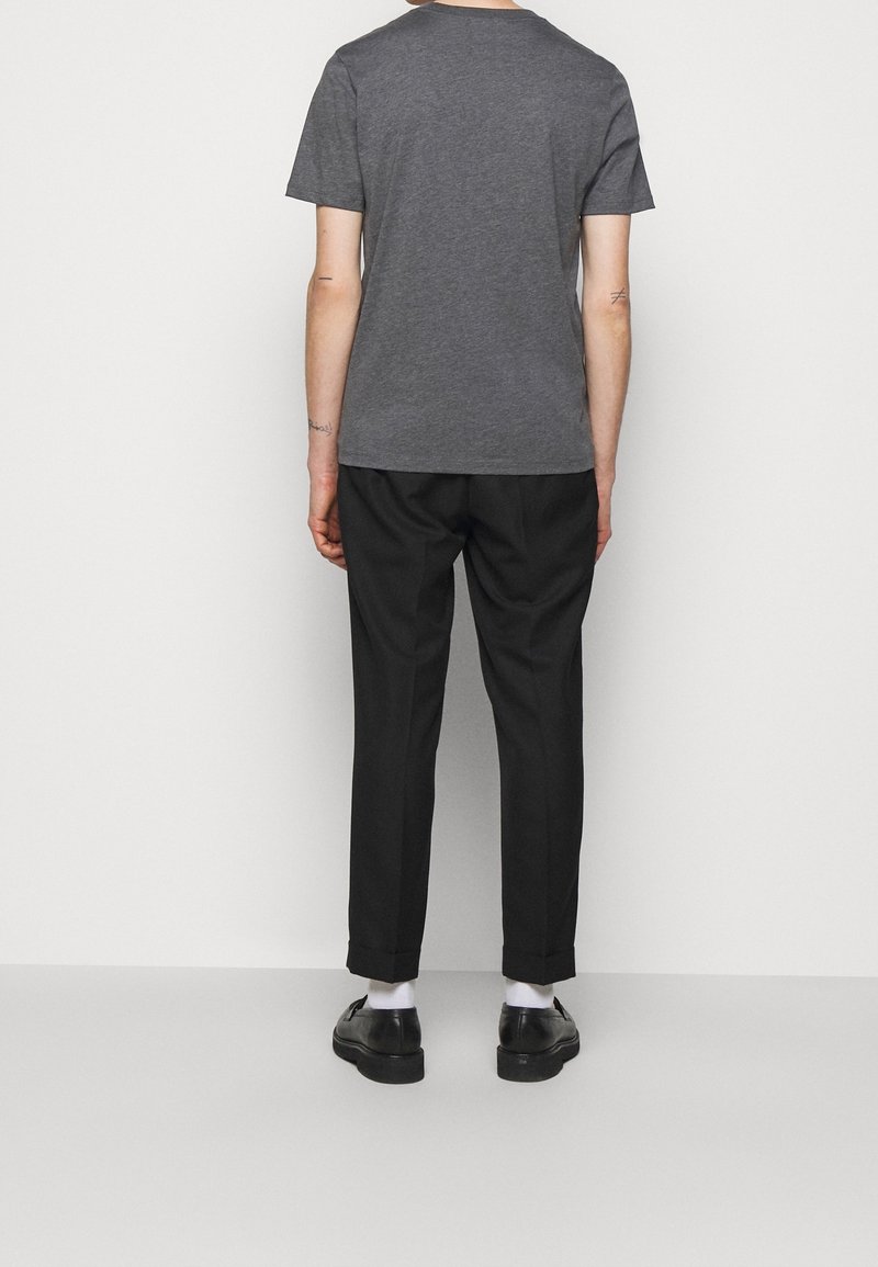 T-shirt en coton gris à manches courtes, associé à un pantalon noir sur mesure, avec les revers retroussés, et des chaussures noires. Design simple et contemporain.