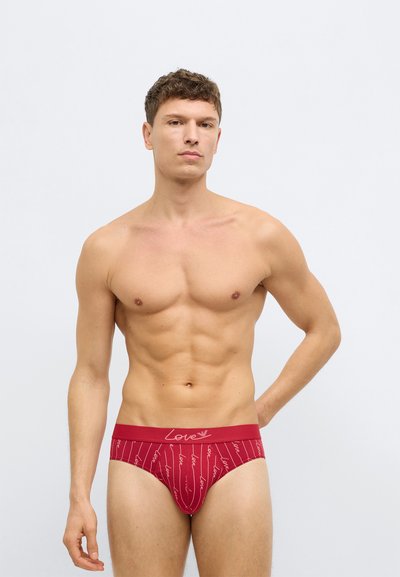Piros pamut alsónadrág kontrasztos derékrésszel, amelyen ismétlődő mintázatban szerepel a "Love" szó. A szövet simának tűnik, finom varrással.