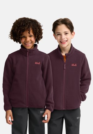 Vestes en polaire bordeaux avec cols hauts et zips complets. Présente le logo Jack Wolfskin en rose sur la poitrine gauche. Portées avec un pantalon noir.