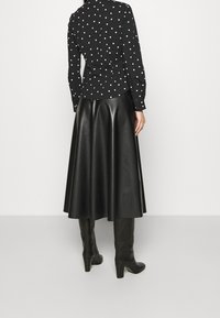 Czarna koszula w białe kropki z dopasowaną talią, w połączeniu z rozkloszowaną czarną skórzaną spódnicą i czarnymi kozakami na wysokim obcasie do kolan.