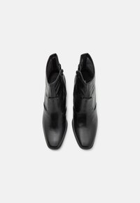 Botines de cuero negro hasta el tobillo con un acabado suave, puntera afilada y cierre de cremallera lateral. Diseño minimalista sin logotipos ni herrajes visibles.