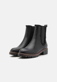 Bottines en cuir noir avec un col en shearling texturé et doux, et une semelle en caoutchouc épaisse. Présente un accent marron autour de la semelle.