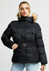 Svart puffjakke med innsvingt midje, hette foret med pels og knappelukking. Har tykk tekstur og justerbart belte med merke.