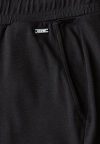 Pantalons de jogging noirs en tissu doux et extensible, dotés d'une taille élastique, de poches latérales et d'un petit logo métallique.