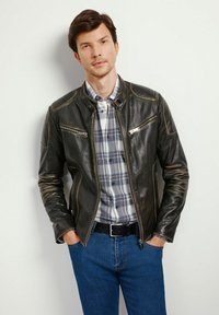 Czarna skórzana kurtka z zamykanymi kieszeniami, dopasowany krój i kontrastowe przeszycia, noszona na koszuli w kratę i niebieskich dżinsach.