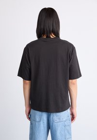 Black cotton t-shirt with a relaxed fit, short sleeves, and a crew neck. Visible stitching along the hem and seamless shoulder design.