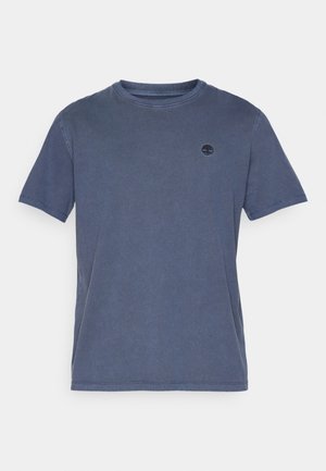 Camiseta de algodón azul con cuello redondo, mangas cortas y un pequeño logo oscuro en el lado izquierdo del pecho. Textura ligeramente desvanecida, corte casual.