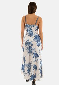 Robe longue sans manches blanche avec un motif floral bleu, dotée de fines bretelles et d'une silhouette fluide. Texture de tissu douce et lisse.