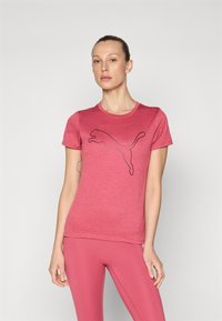 Rosa, kortermet T-skjorte laget av strukturert stoff, med et stort svart Puma-logo foran, båret med matchende rosa leggings.