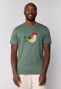 T-shirt vert à manches courtes en coton avec un design géométrique d'oiseau en rouge, jaune, vert et noir sur le devant.