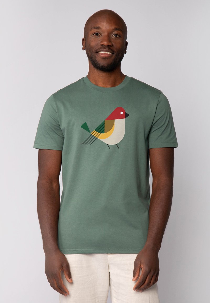 T-shirt vert à manches courtes en coton avec un design géométrique d'oiseau en rouge, jaune, vert et noir sur le devant.