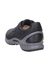 Scarpa atletica nera in pelle con un collare imbottito, suola in gomma grigia e un design elegante. Presenta una punta rotonda e pochi dettagli.