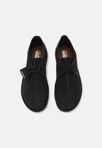 Chaussures en cuir suédé noir avec un design simple, comportant une couture centrale, un bout rond, un laçage et une semelle en caoutchouc.