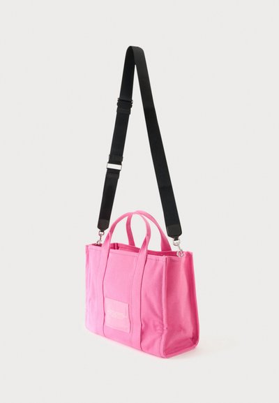 Sac fourre-tout rectangulaire rose avec double poignée et une longue bandoulière noire réglable sur fond blanc.