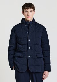 Giacca a vento trapuntata blu navy con colletto alto, due tasche frontali e bottoni abbinati. Tessuto leggero con una consistenza liscia.