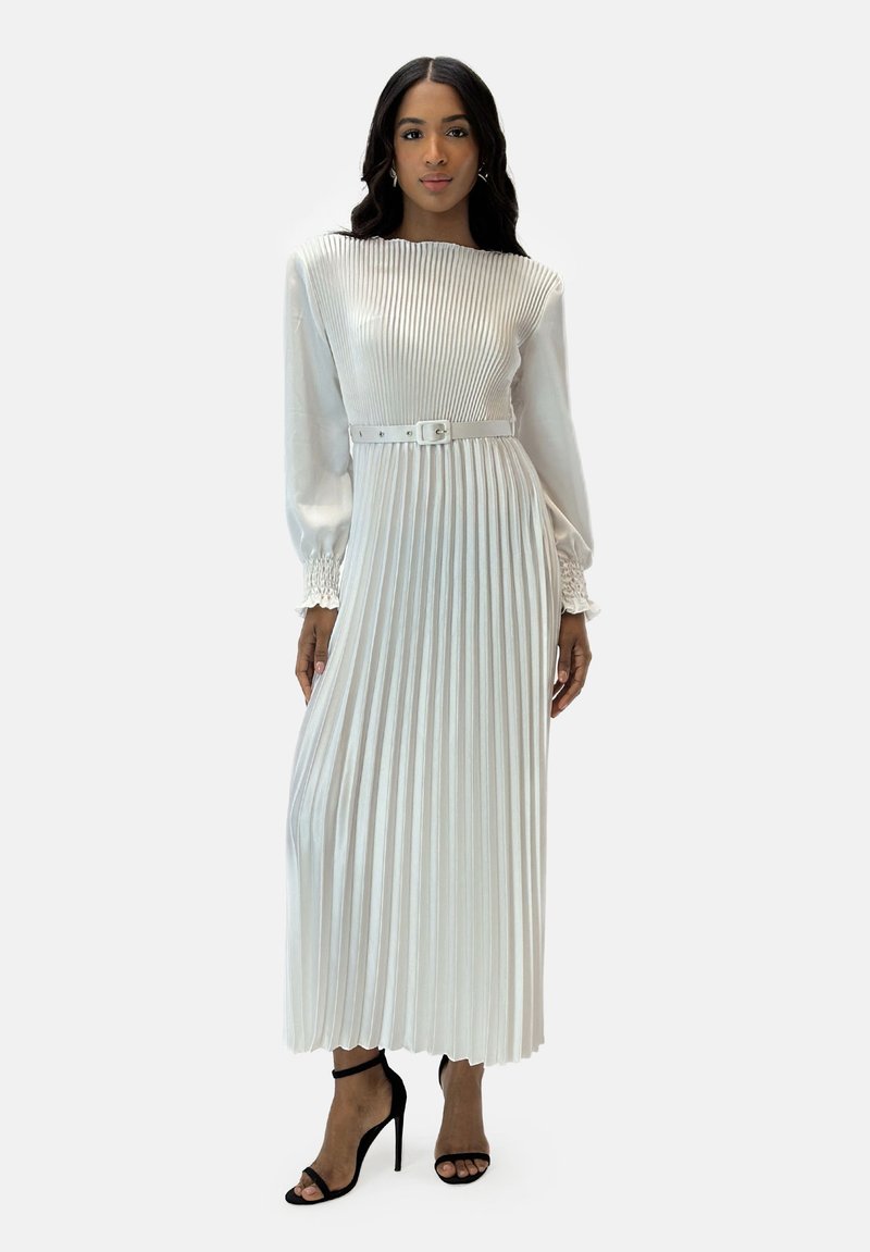 Witte geplooide maxi-jurk met een aansluitende bodice, lange pofmouwen, een ceintuur in de taille en zwarte hoge haksandalen. Glad, gestructureerd materiaal.