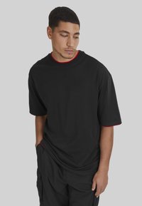 Camiseta negra de manga corta con cuello redondo y ribete rojo, de corte relajado y fabricada en suave algodón. Se lleva con pantalones cargo negros.