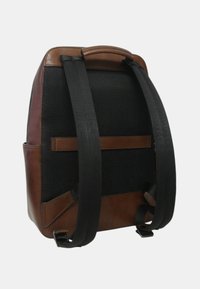 Zaino in pelle marrone e rete nera con spallacci neri imbottiti e una maniglia superiore, mostrato dal retro su uno sfondo bianco.