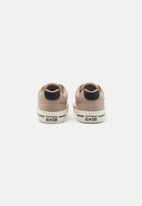 Béžové kožené tenisky s námorníckym akcentom na pätách a bielou gumovou podošvou. Na zadnej strane sa nachádza branding "CONVERSE ALL STAR".