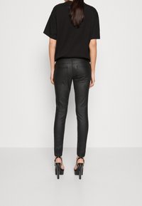 Svarta läderbyxor i slim fit med en slät yta, utrustade med två bakfickor och en hög midja, tillsammans med svarta högklackade skor.