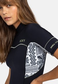 Combinaison de plongée noire à manches courtes, avec un panneau latéral à motif en blanc et noir. Accents en vert fluo, mettant en avant le logo de la marque.