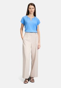 Jasnoniebieska plisowana bluzka z dekoltem w kształcie klucza, zestawiona z jasnobeżowymi szerokimi spodniami i czarnymi sandałami na szpilce. Gładkie faktury i luźny krój.