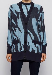 Blå och marinblå mönstrad cardigan med v-ringning, långa ärmar, framfickor och sex svarta knappar framtill. Mjuk stickad textur.