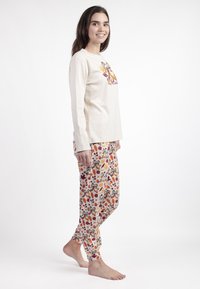 Camiseta de manga larga color beige claro con gráfico de dibujos animados. Pantalones de pijama de tela ligera estampada en colores otoñales con hojas y personajes divertidos.