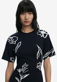 Schwarzes T-Shirt mit kurzen Ärmeln, das mit weißen Blumen- und Blättermotiven verziert ist. Hergestellt aus einem weichen Stoff, mit Rundhalsausschnitt und lockerer Passform.