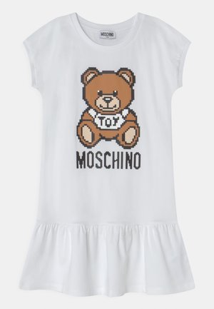 Biała sukienka z krótkim rękawem i falbaną u dołu, z pikselowym brązowym misiem w koszulce z napisem "TOY" oraz napisem "MOSCHINO" poniżej.
