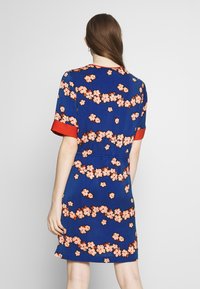 Bloemjurk met een blauwe achtergrond en roze en witte bloemenpatronen, rode omgeslagen korte mouwen en elastische taille.