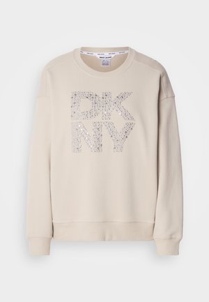 Beige genser med rund hals og lange ermer. Har en glitrende "DKNY" logo laget av rhinestener på fronten. Myk tekstur.