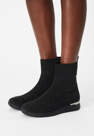 Botines negros hasta el tobillo hechos de material tejido que presentan un diseño texturizado con pequeños puntos brillantes y una suela negra lisa con herrajes metálicos.