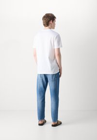 Camiseta blanca de manga corta, de corte relajado, combinada con vaqueros de mezclilla azul claro. Sandalias negras completan el look. Diseño simple y casual.