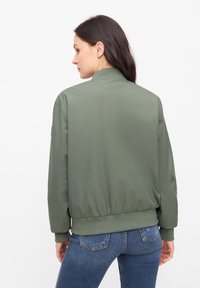 Grön bomberjacka med ståkrage, elastiska mudd och nederkant. Slät tygkvalitet, med en enkel design utan synliga mönster.