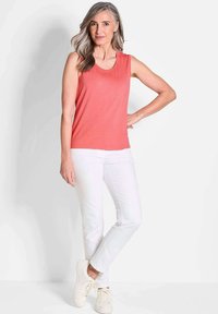 Koraal kleurige mouwloze top, zachte stof, ronde halslijn; gecombineerd met witte slim-fit broek en beige sneakers. Eenvoudige en moderne outfit.