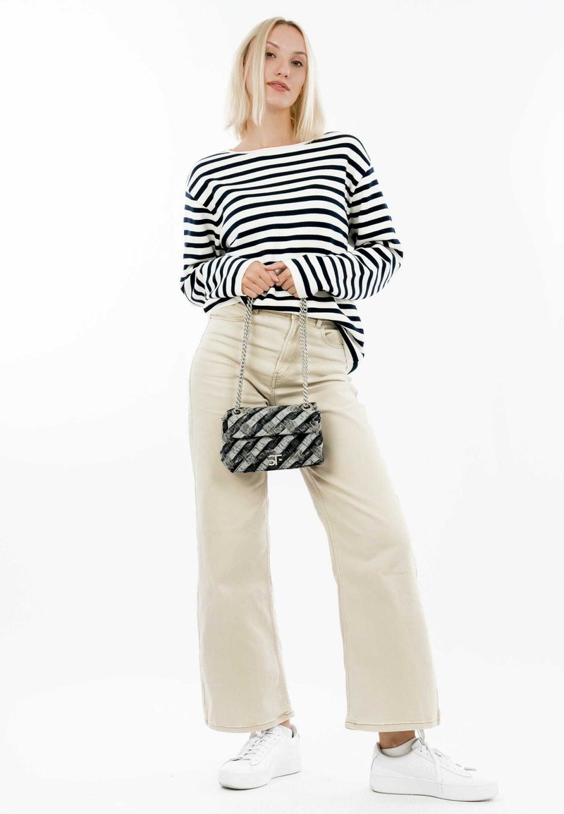 Camicia a maniche lunghe a righe bianche e nere, pantaloni beige a gamba larga, sneakers bianche e una borsa nera texturizzata con tracolla a catena.