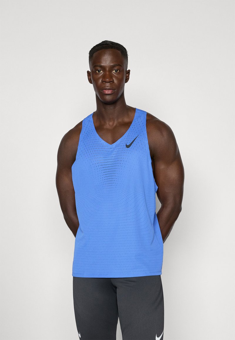 Niebieski top na ramiączkach marki Nike z dekoltem w kształcie litery V, siatkową teksturą i czarnym logo. Połączony z szarymi spodniami sportowymi.