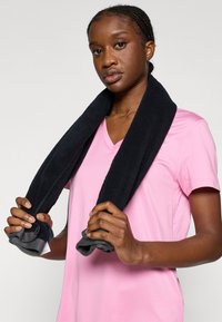 Čierny uterák prehodený cez plecia, nosený s ružovým tričkom s výstrihom do V. Uterák má textúrovaný povrch; tričko je hladké a ľahké.