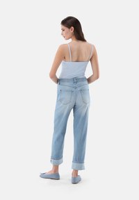 Hellblaues Tanktop mit dünnen Trägern, kombiniert mit hellen Jeans mit umgeschlagenen Säumen und Stickdetails. Passende hellblaue Ballerinas.