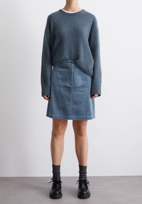 Suéter de punto azul con mangas largas, combinado con una falda de pana azul clara que presenta un botón frontal y bolsillos. Zapatos negros con cordones y calcetines grises.