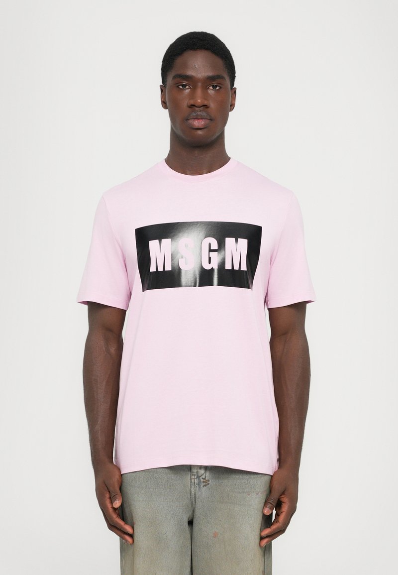 Kortermet rosa t-skjorte med et svart rektangulært grafikk med "MSGM" i hvite bokstaver. Mykt bomullsmateriale, avslappet passform.