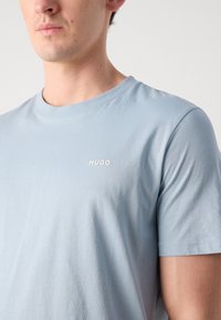 T-shirt in cotone azzurro chiaro con maniche corte, scollo a girocollo e un piccolo logo bianco "HUGO" sul petto. Tessuto morbido e vestibilità comoda.