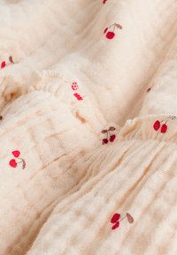 Tissu en coton de couleur crème douce avec des ondulations texturées, orné de broderies de cerises rouges et de tiges marron tout au long.