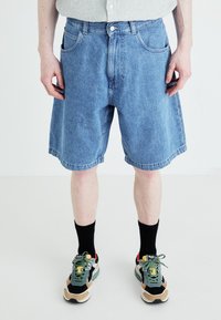 Shorts en denim bleu avec une coupe décontractée, dot�és d'une fermeture à bouton, de poches avant et d'un ourlet plat, associés à des baskets multicolores et des chaussettes noires.